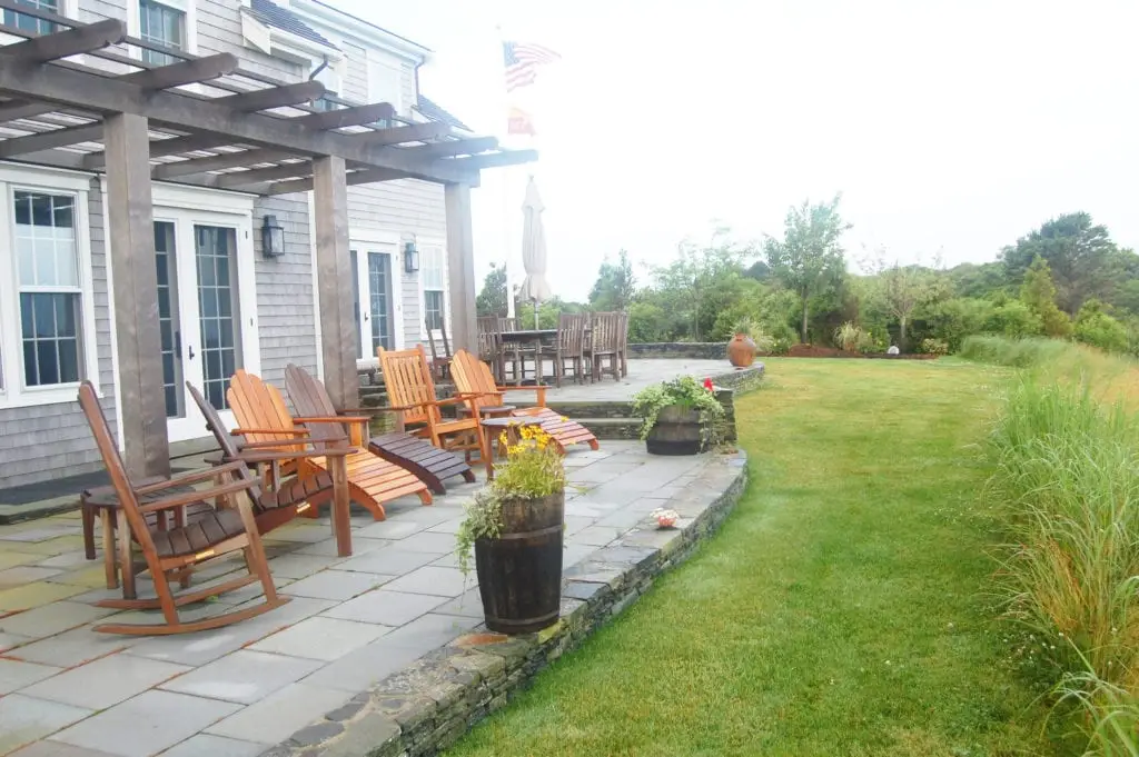 patio with stone walls beneath a pergola in back yard garden setting with tall grasses